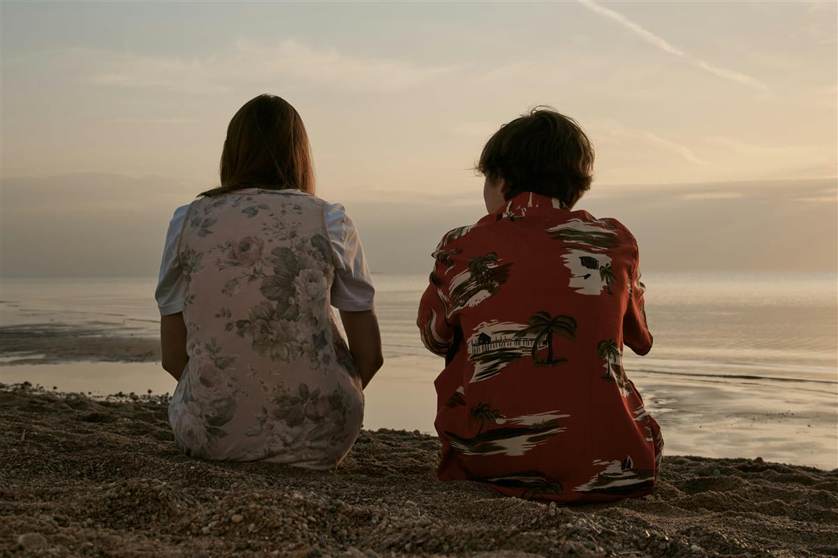 To personer sitter med ryggen til og ser ut mot havet - Klikk for stort bilde